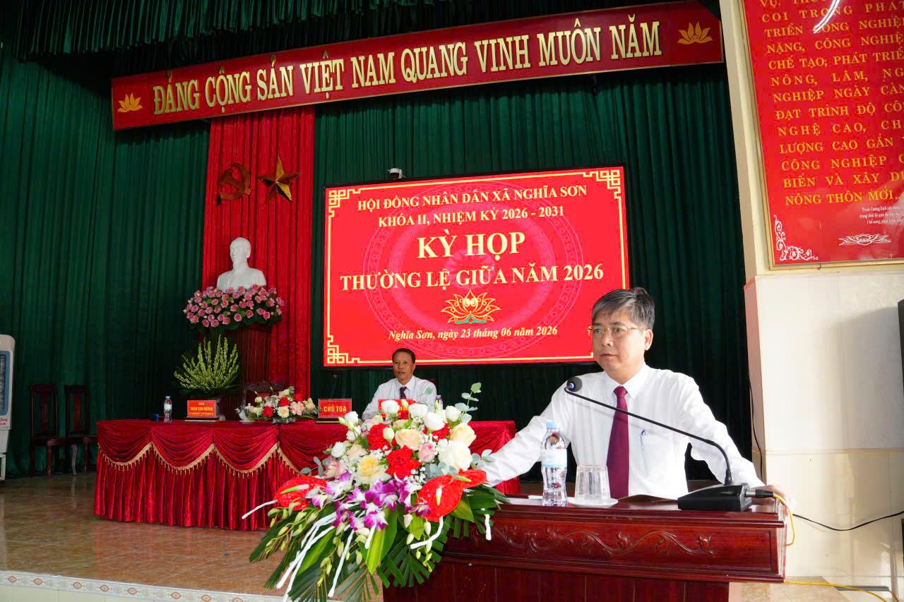 A person standing at a podium with a microphone and flowers Description automatically generated
